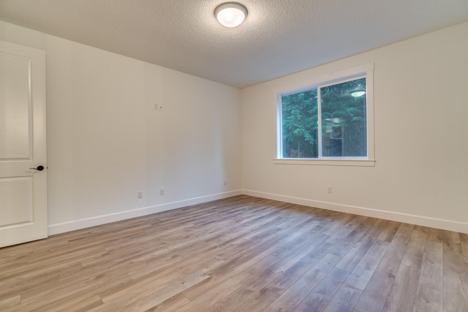 An empty bedroom with hardwood floors and a window.