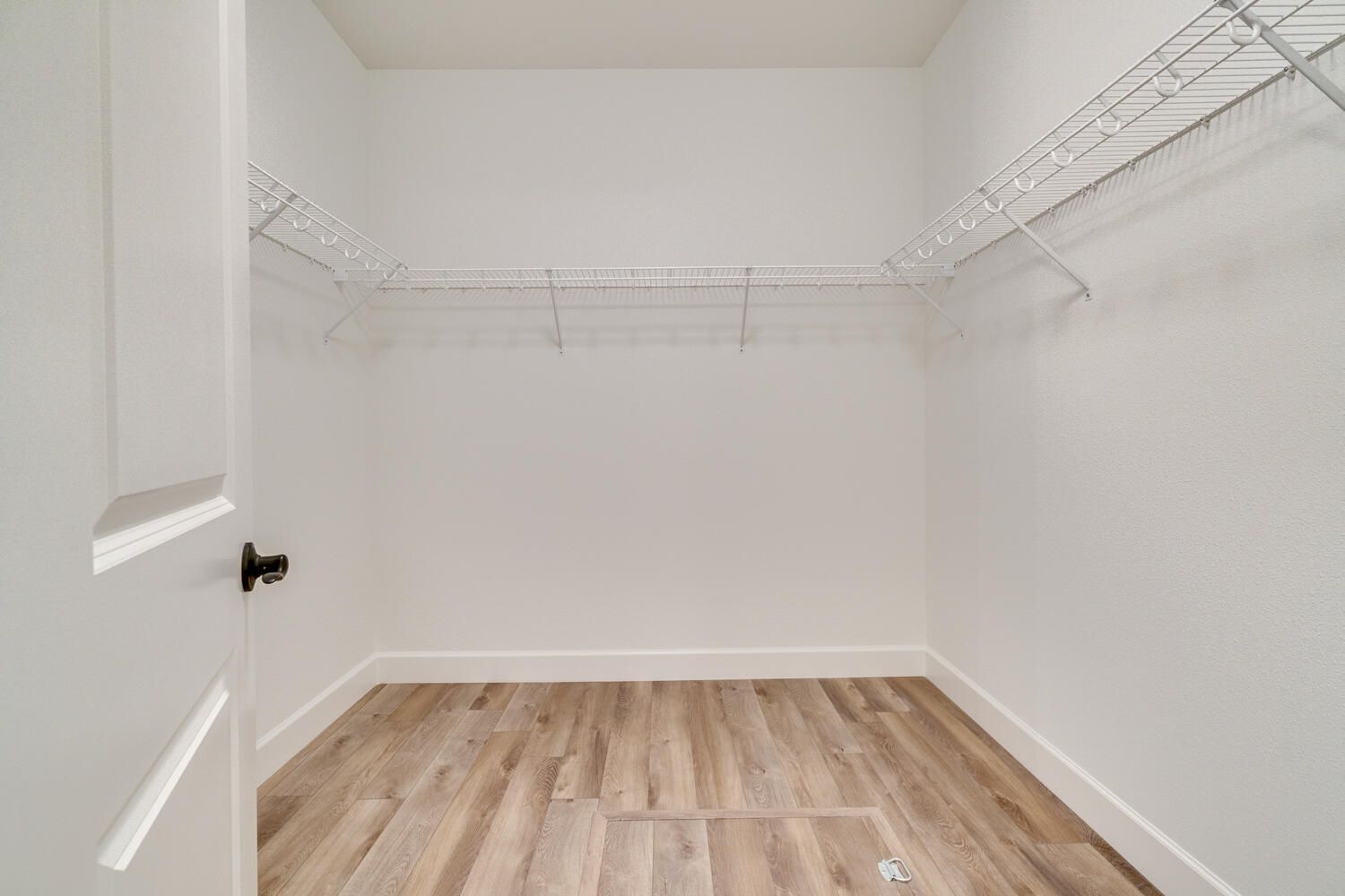 An empty walk in closet with hardwood floors and white walls.