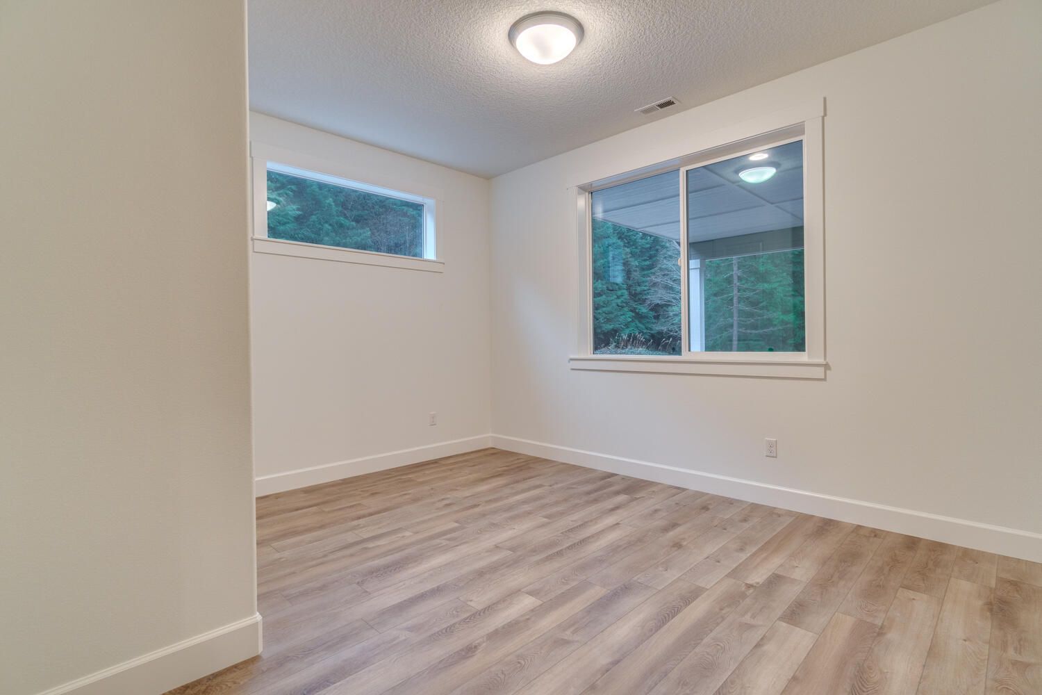 An empty room with hardwood floors and two windows.