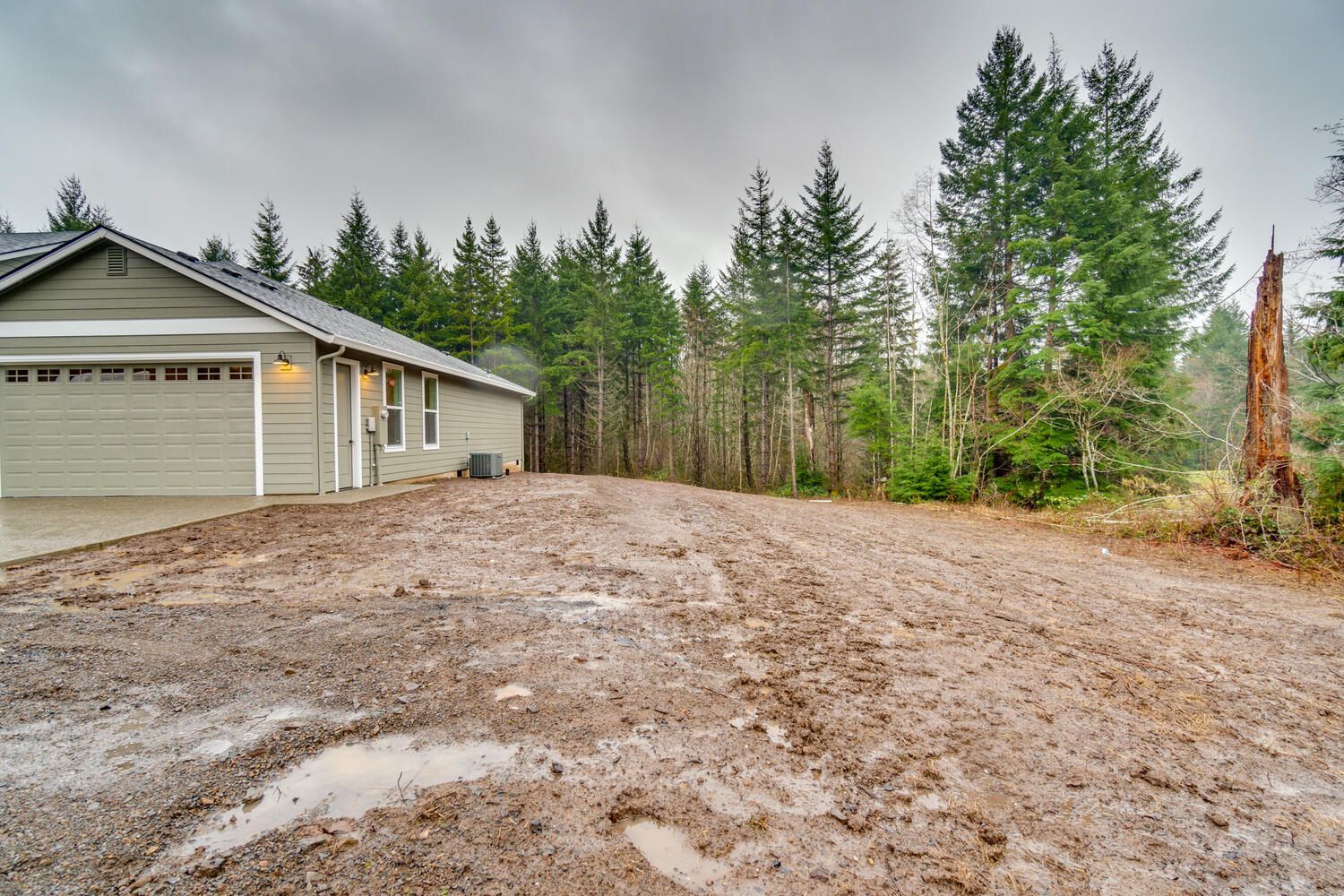 A muddy driveway in front of a house with trees in the background