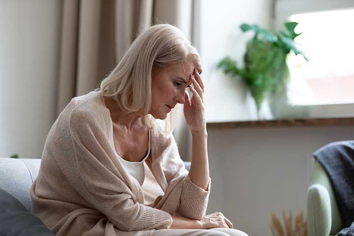 Sad mature woman sitting alone at home feeling headache depression 
