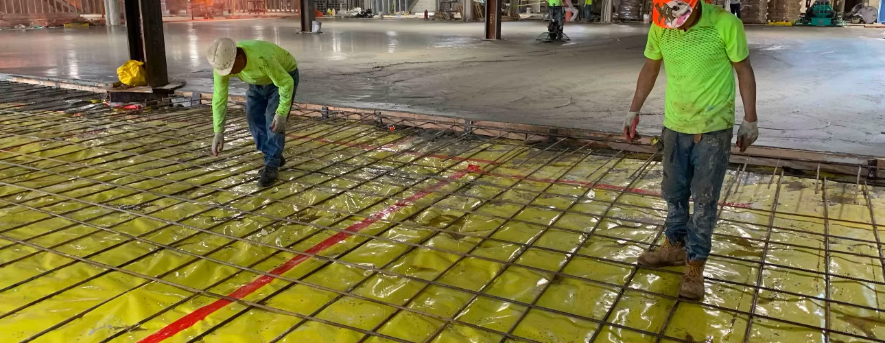 Construction workers pouring and leveling concrete over rebar for a commercial building foundation.