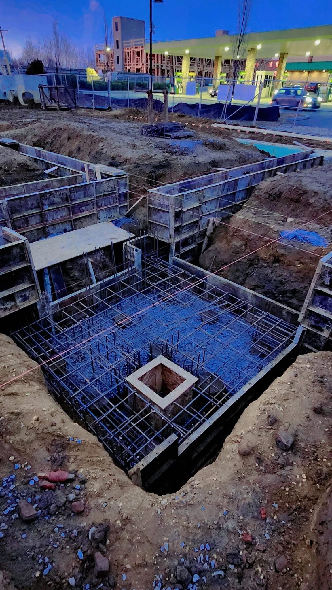 Evening view of a construction site with foundation framing and utility trench preparation.