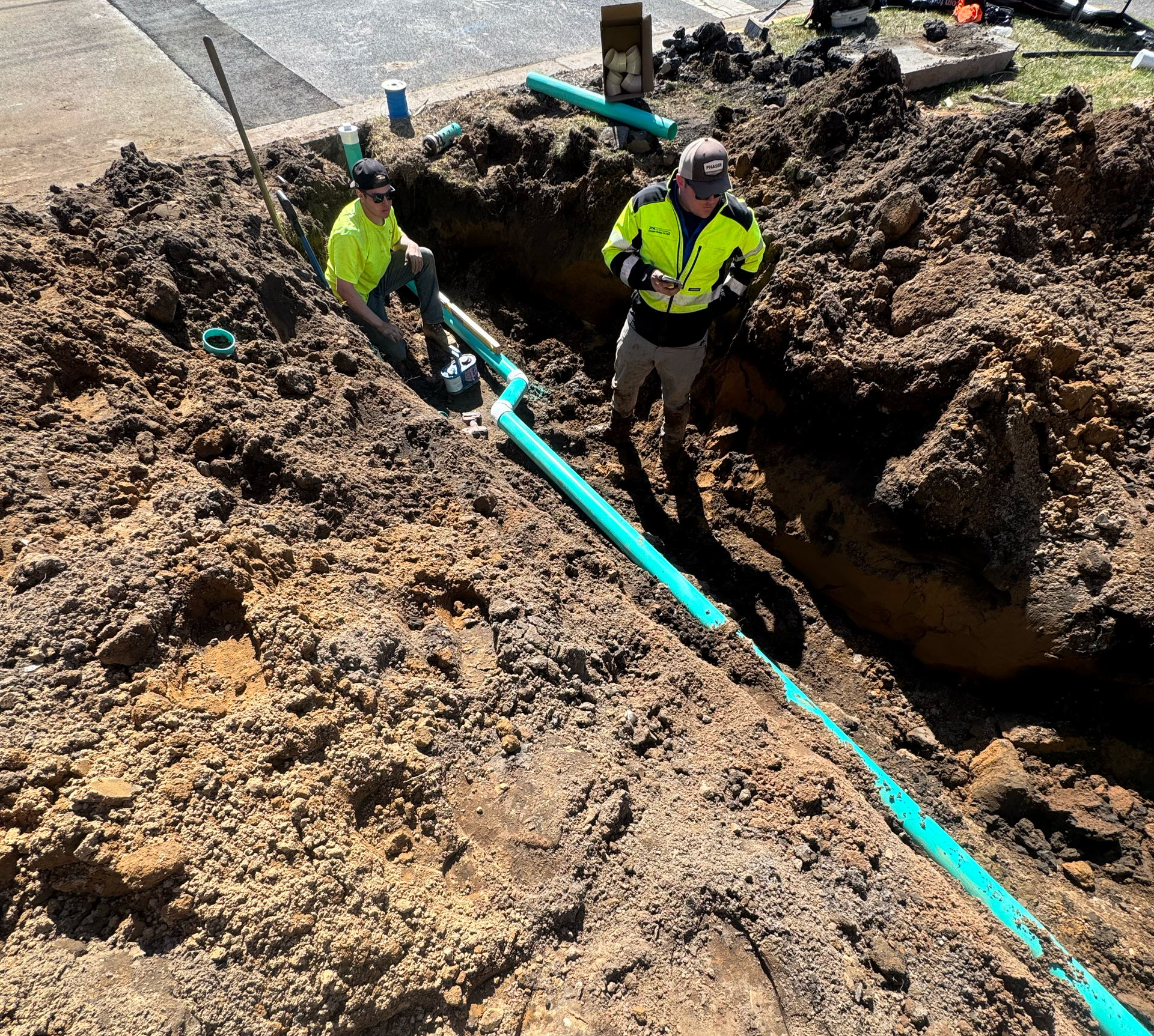 Construction crew installing underground water or sewer piping inside a deep trench.