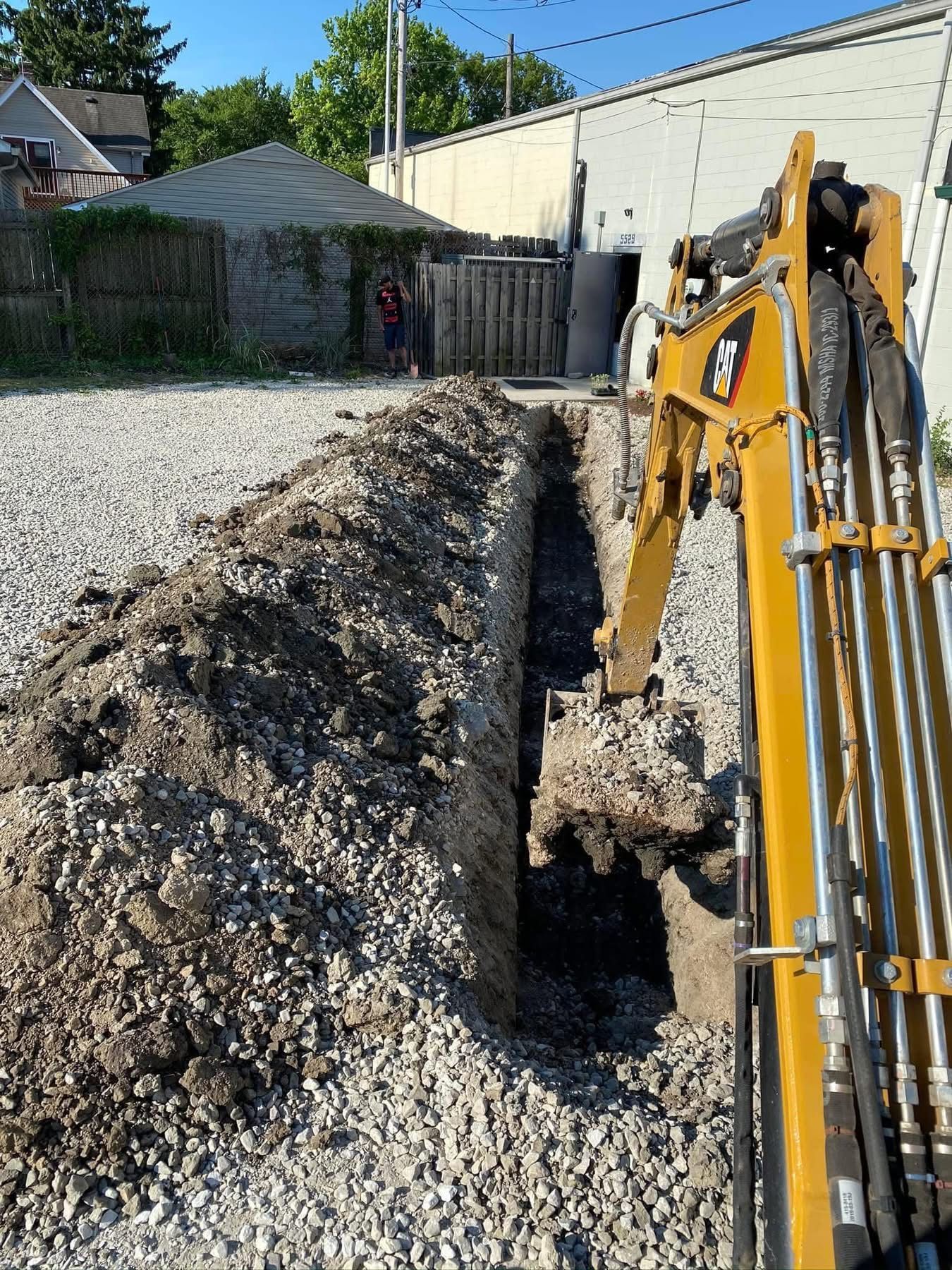 Excavator preparing a trench for underground utility installation alongside a commercial building.