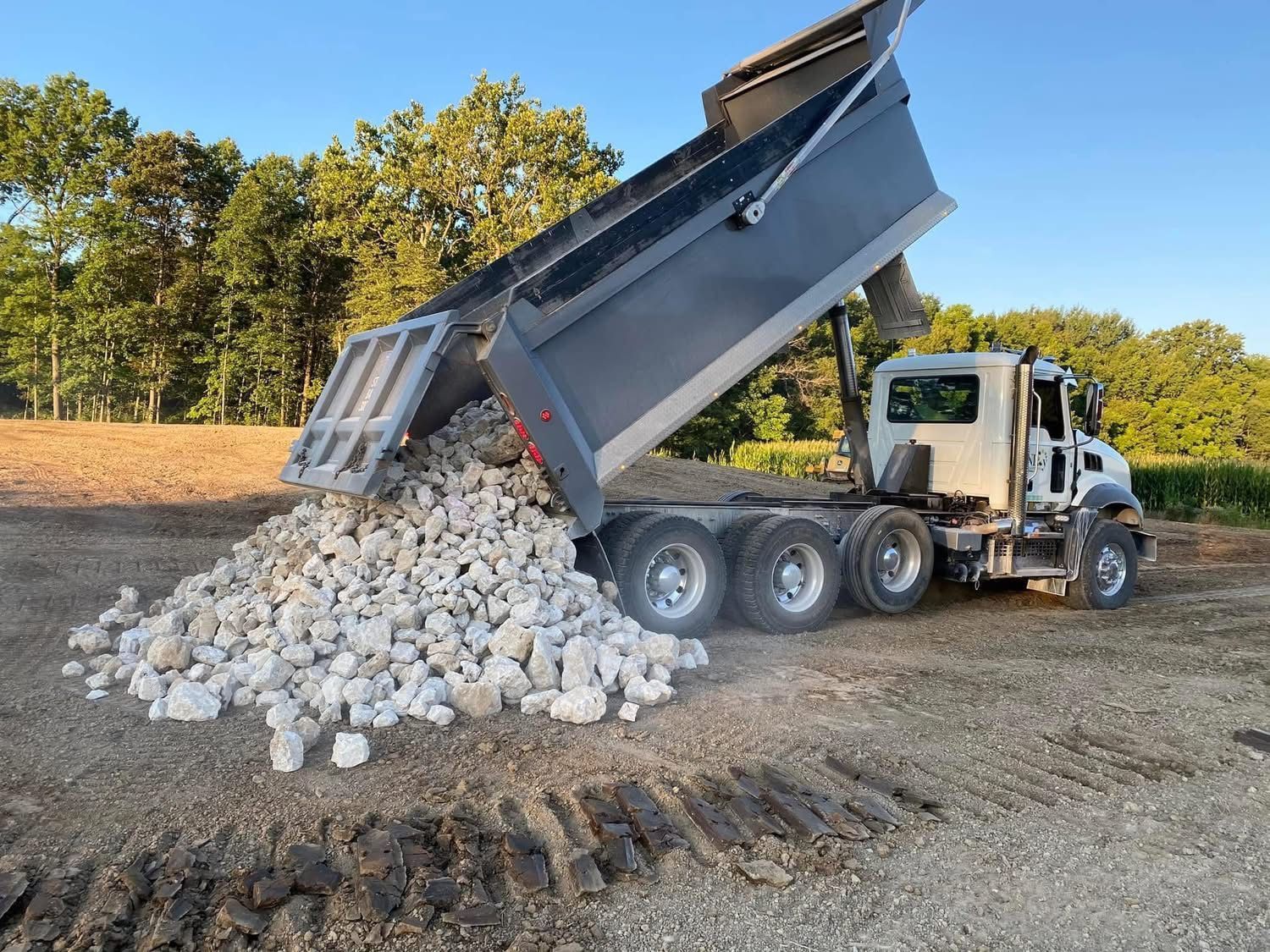 Dump truck unloading large stones for site grading, drainage, or foundation support.