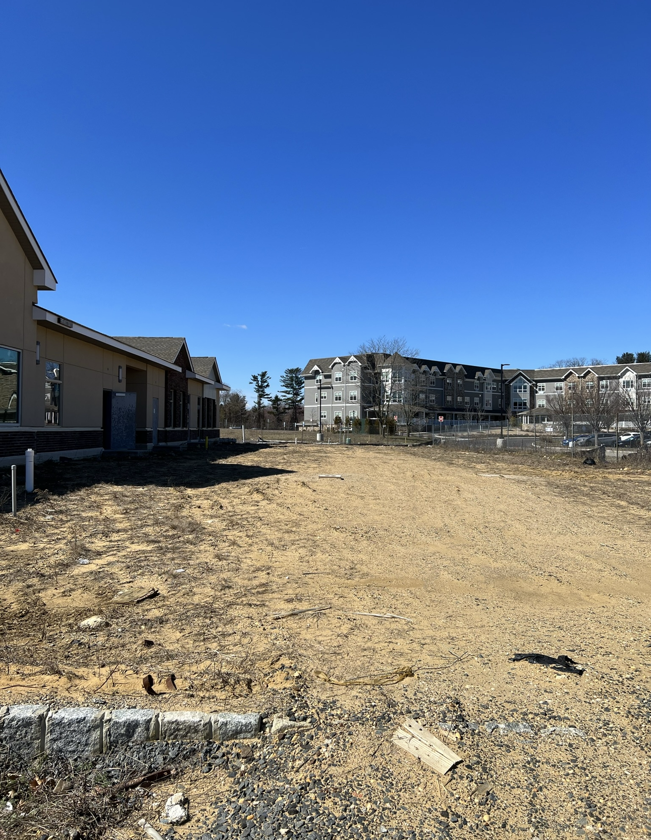 Wide view of a construction site under a clear blue sky with active development nearby.