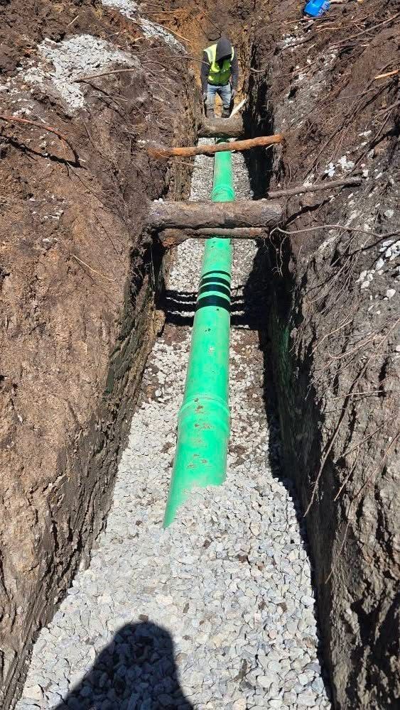 Worker installing underground piping and utility infrastructure inside a freshly excavated trench.