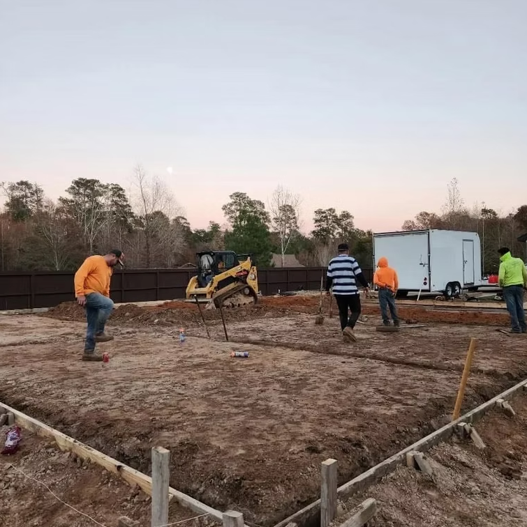 Workers on site during a late-day construction project with foundation preparation underway.