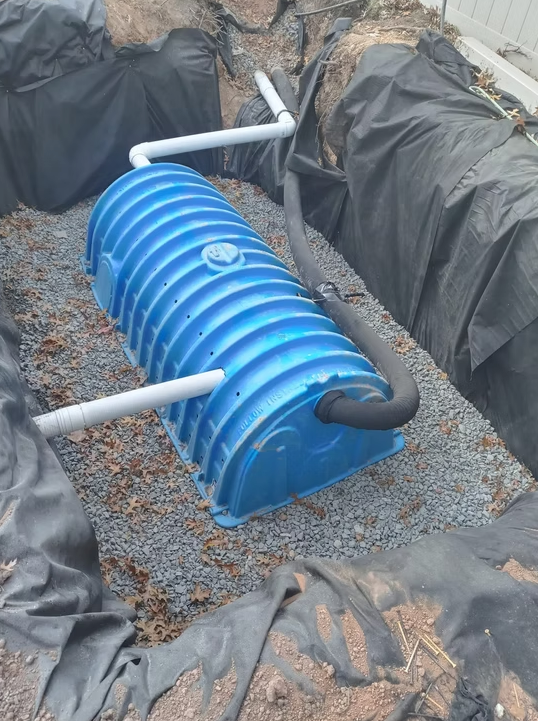 Blue underground utility tank installation with drainage connections during residential infrastructure work.