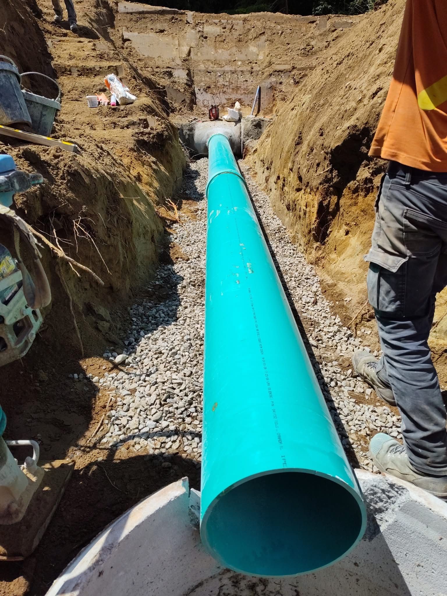 Crew installing a large green sewer pipe within a deep trench for underground infrastructure development.