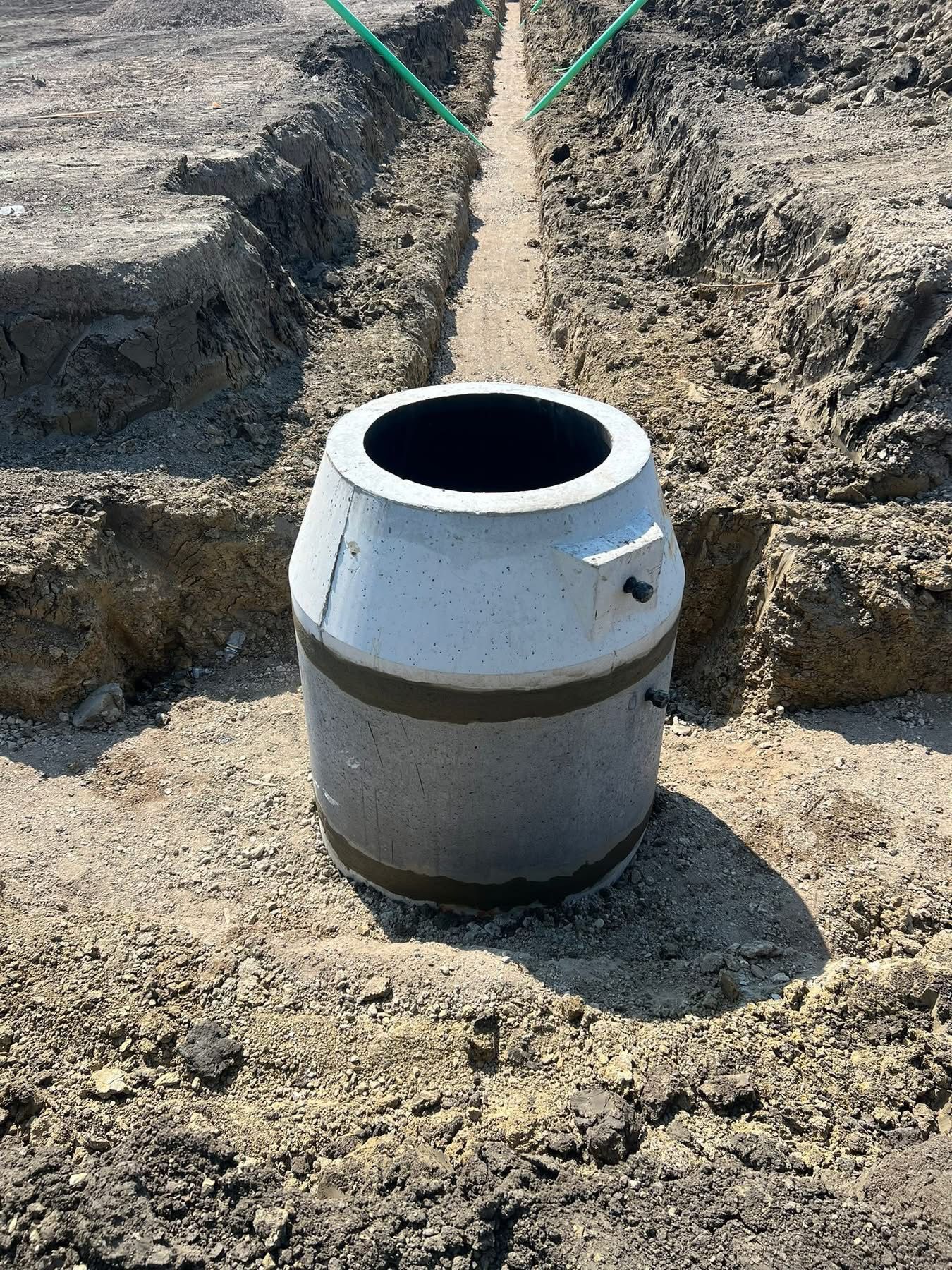 Concrete manhole base positioned for underground utility system installation and stormwater drainage.