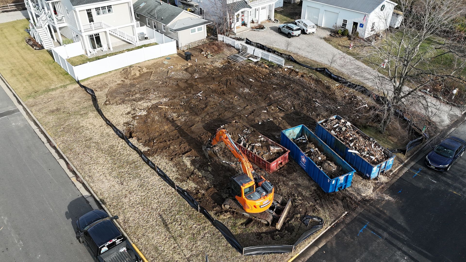 Drone view of residential site excavation with heavy equipment and debris removal containers.