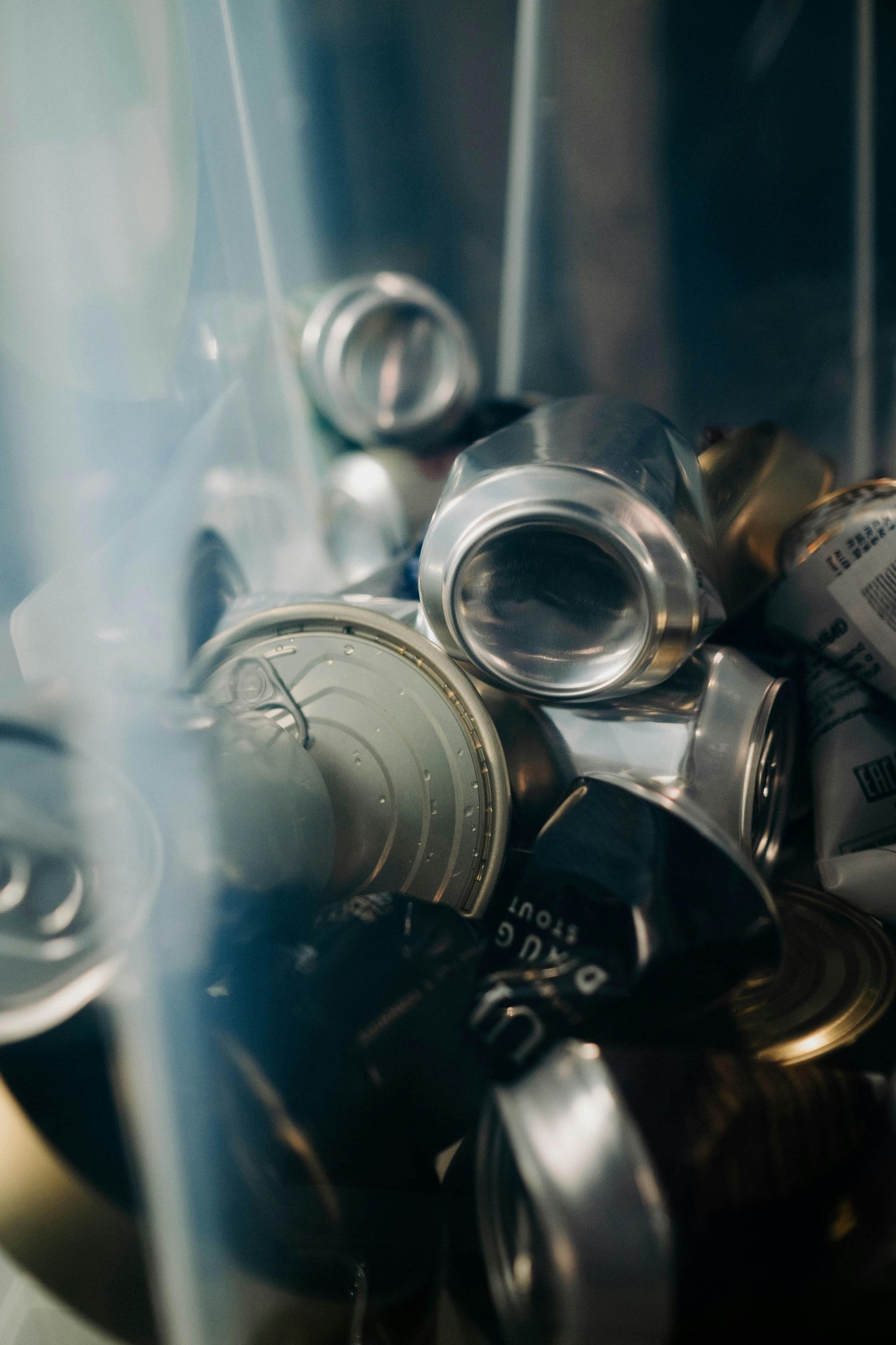 Crushed aluminum cans inside a clear recycling bin, with a focus on the openings and torn tops.