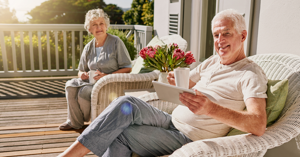 Smiling retirees relaxing outdoors with coffee and tablet, representing concierge medicine lifestyle