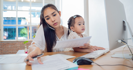 Busy parent working at a computer while holding a child, illustrating how telemedicine and virtual m