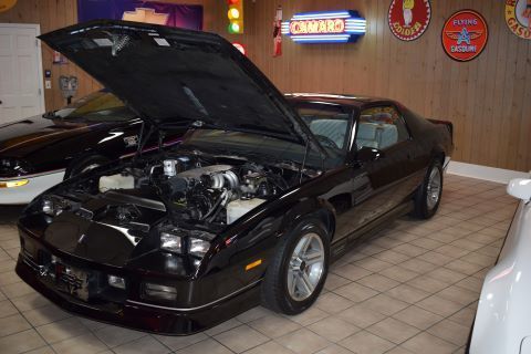 A black car with the hood up is parked in a garage.