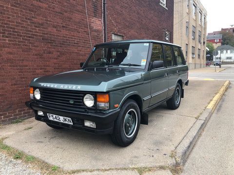 A range rover is parked on the side of the road in front of a brick building.