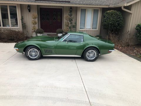 A green corvette is parked in a driveway in front of a house.