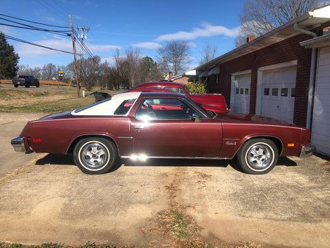 A red car with a white top is parked in front of a garage.