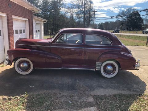 An old car is parked in front of a garage.