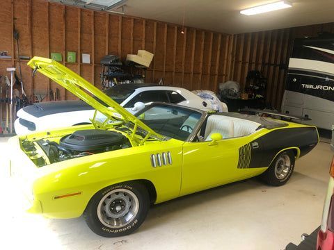 A yellow convertible is parked in a garage with its hood up.