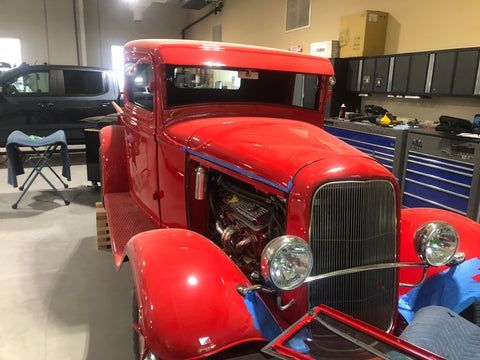 A red car is sitting in a garage with the hood open.
