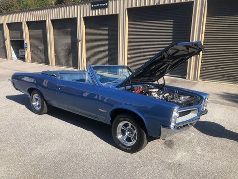 A blue convertible with the hood up is parked in front of a garage.