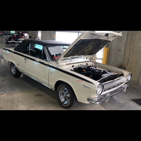 A white car with the hood up is parked in a garage.