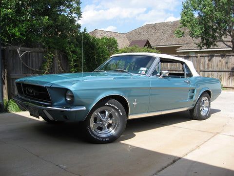 A blue mustang with a white top is parked in a driveway.