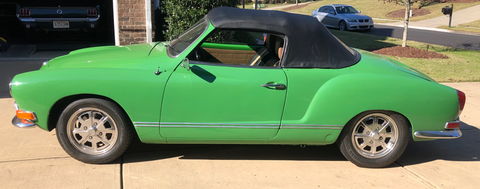 A green car with a black top is parked in a driveway.