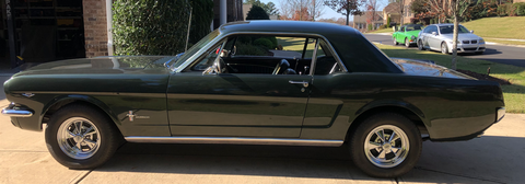 A green mustang is parked in a driveway next to a garage.