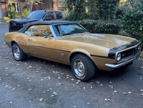 A gold car with a black top is parked in a driveway.