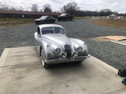 A silver car is parked in a gravel lot.