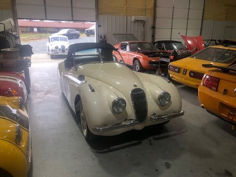A white sports car is parked in a garage next to other cars.