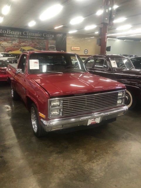 A red truck is parked in a showroom with other cars.