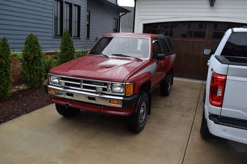 A red toyota hilux is parked in a driveway next to a white truck.