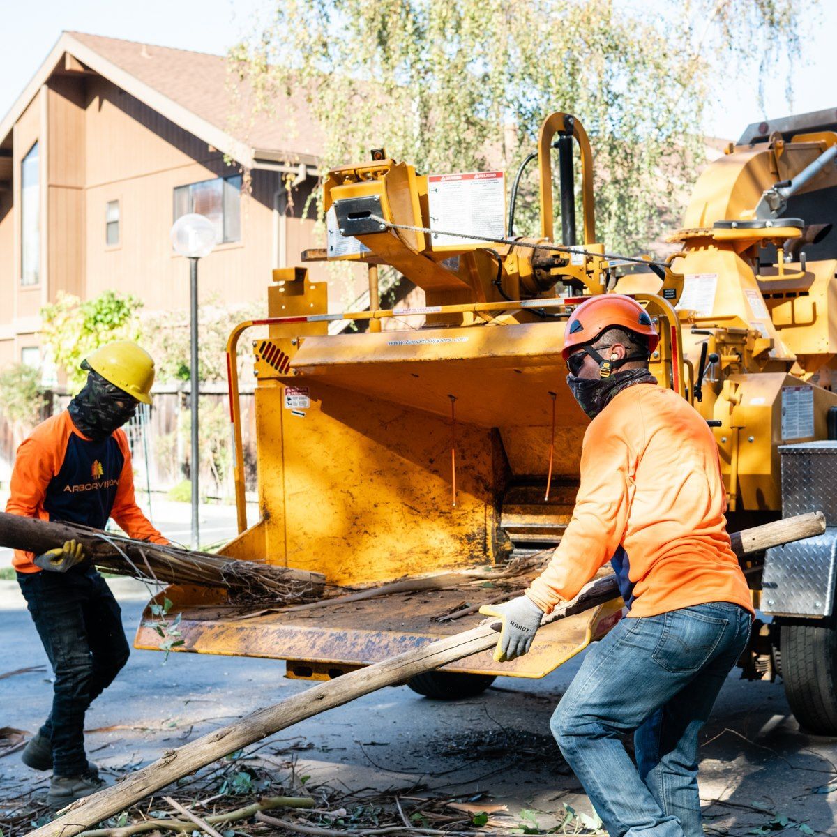 Two men wearing hard hats are pushing a tree chipper