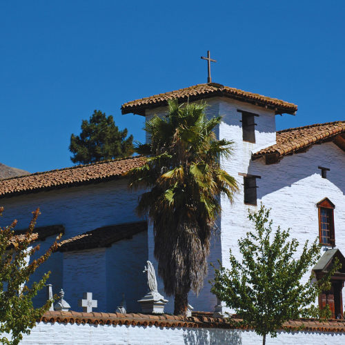 Mission San Jose in Fremont, CA, with a palm tree and whitewashed walls.