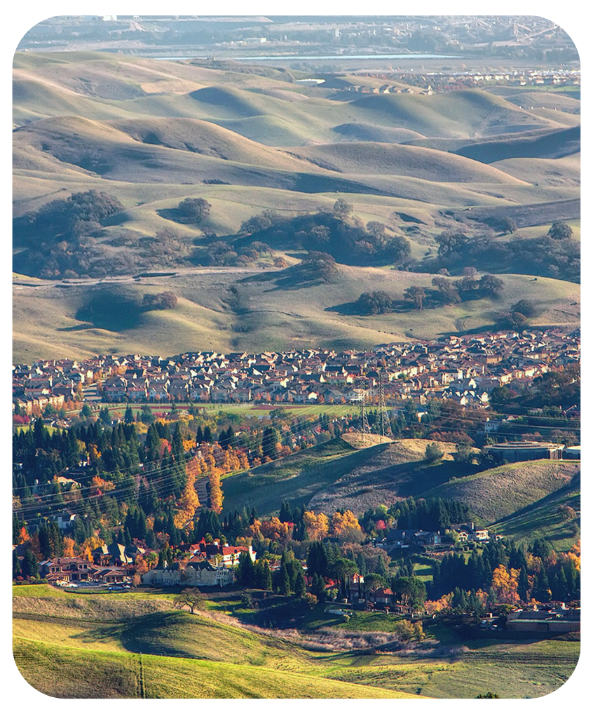 Scenic view of rolling green hills near Mount Diablo, with a suburban neighborhood nestled at the foothills surrounded by vibrant autumn foliage.