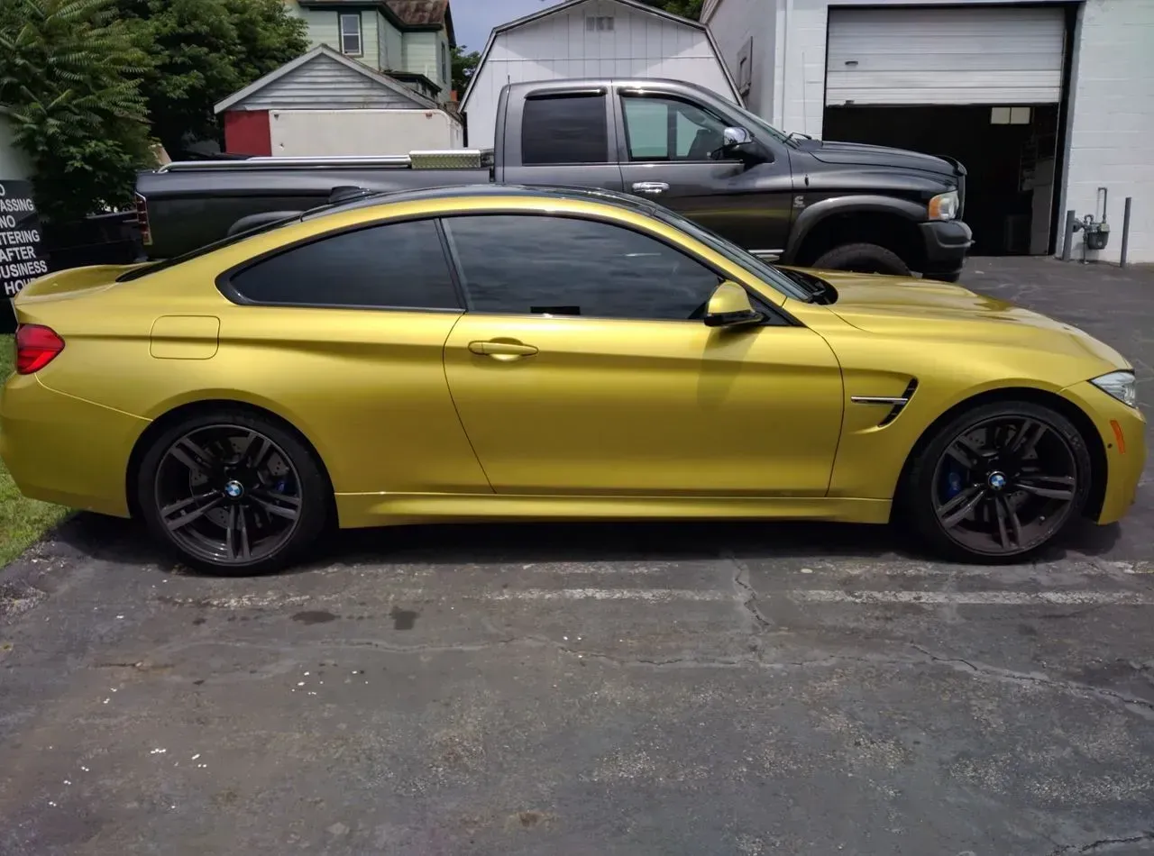 A yellow bmw is parked in a parking lot next to a truck.