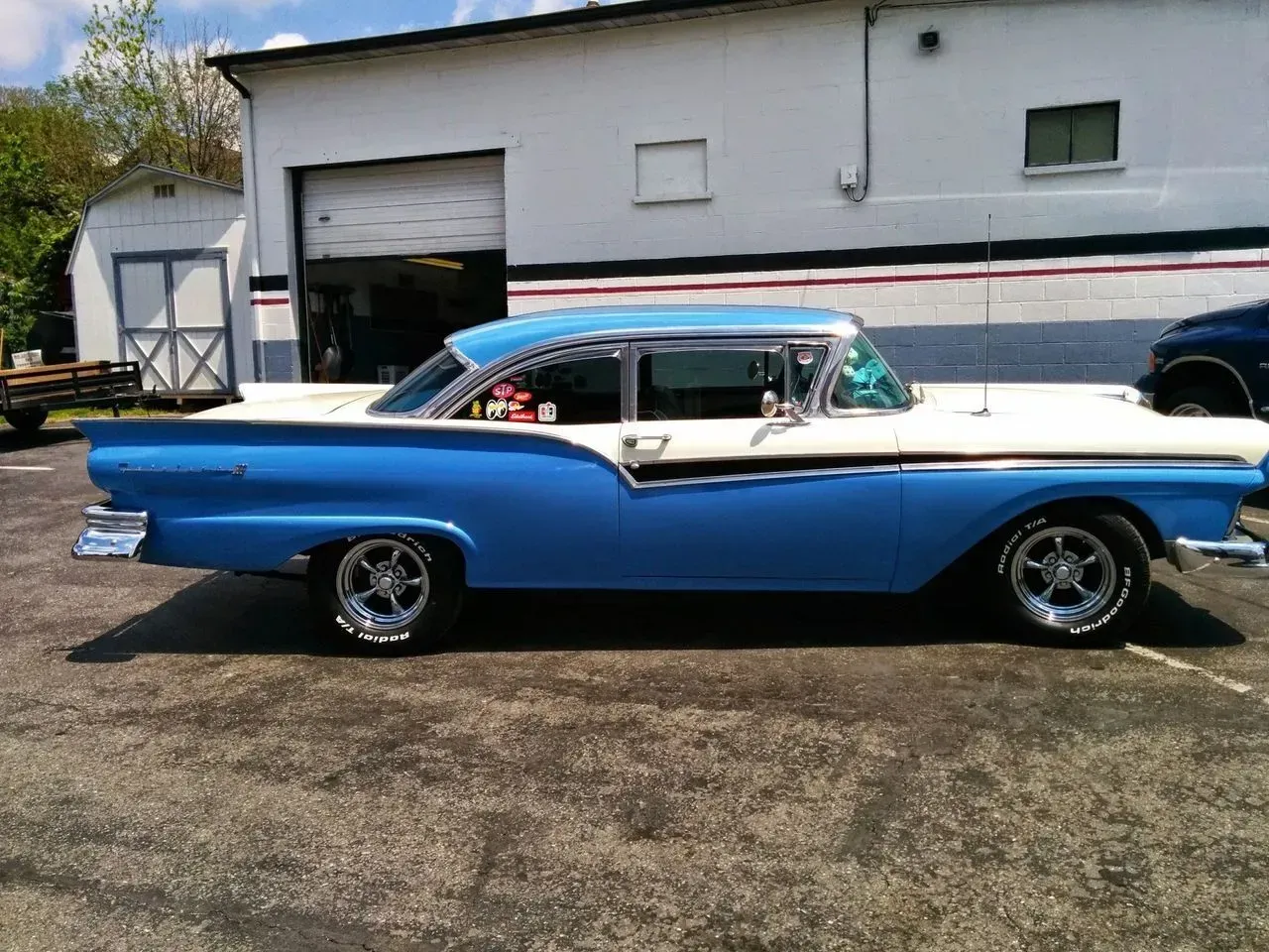 A blue and white car is parked in front of a garage.