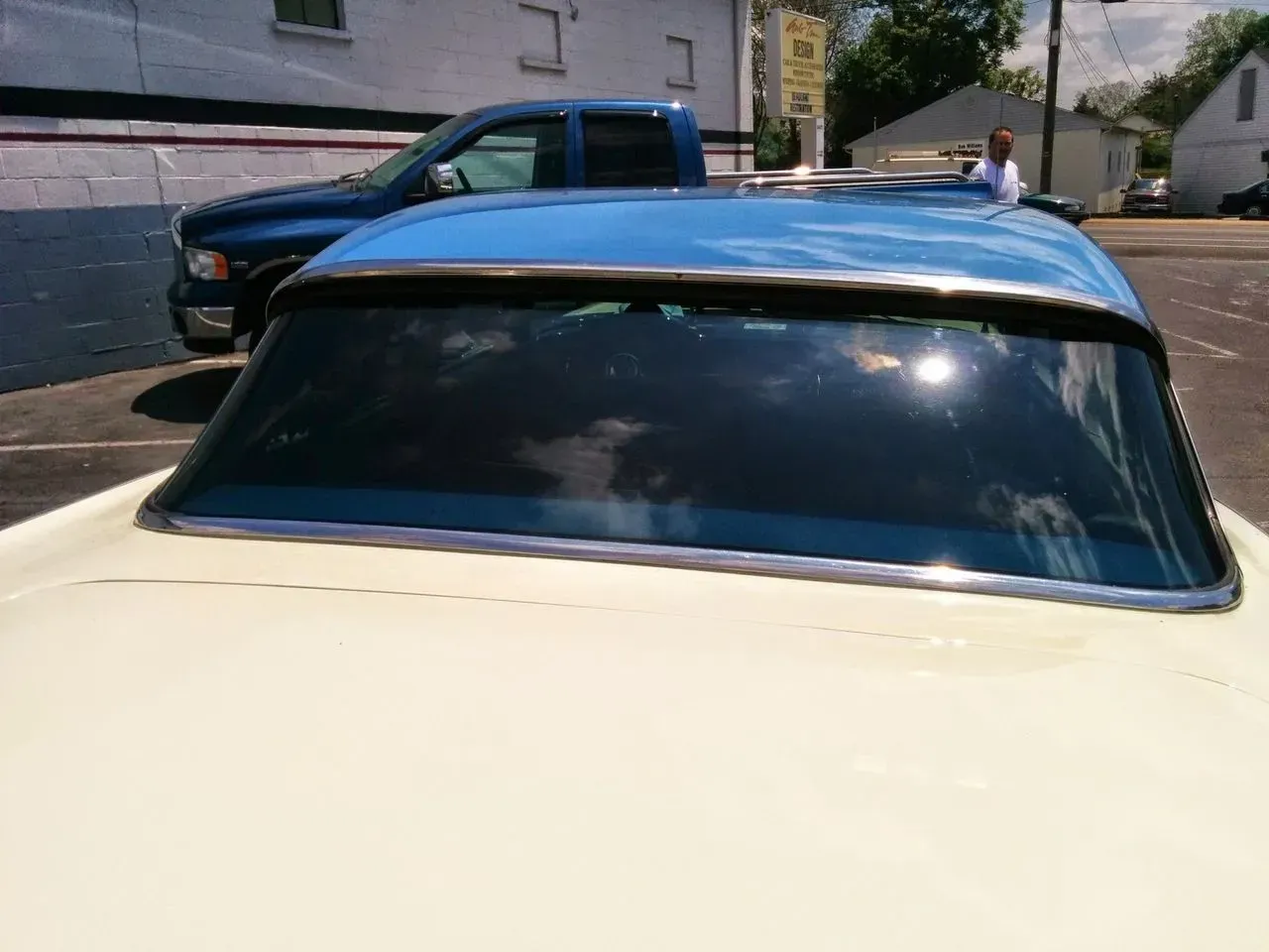 A white car with a blue roof is parked in a parking lot.