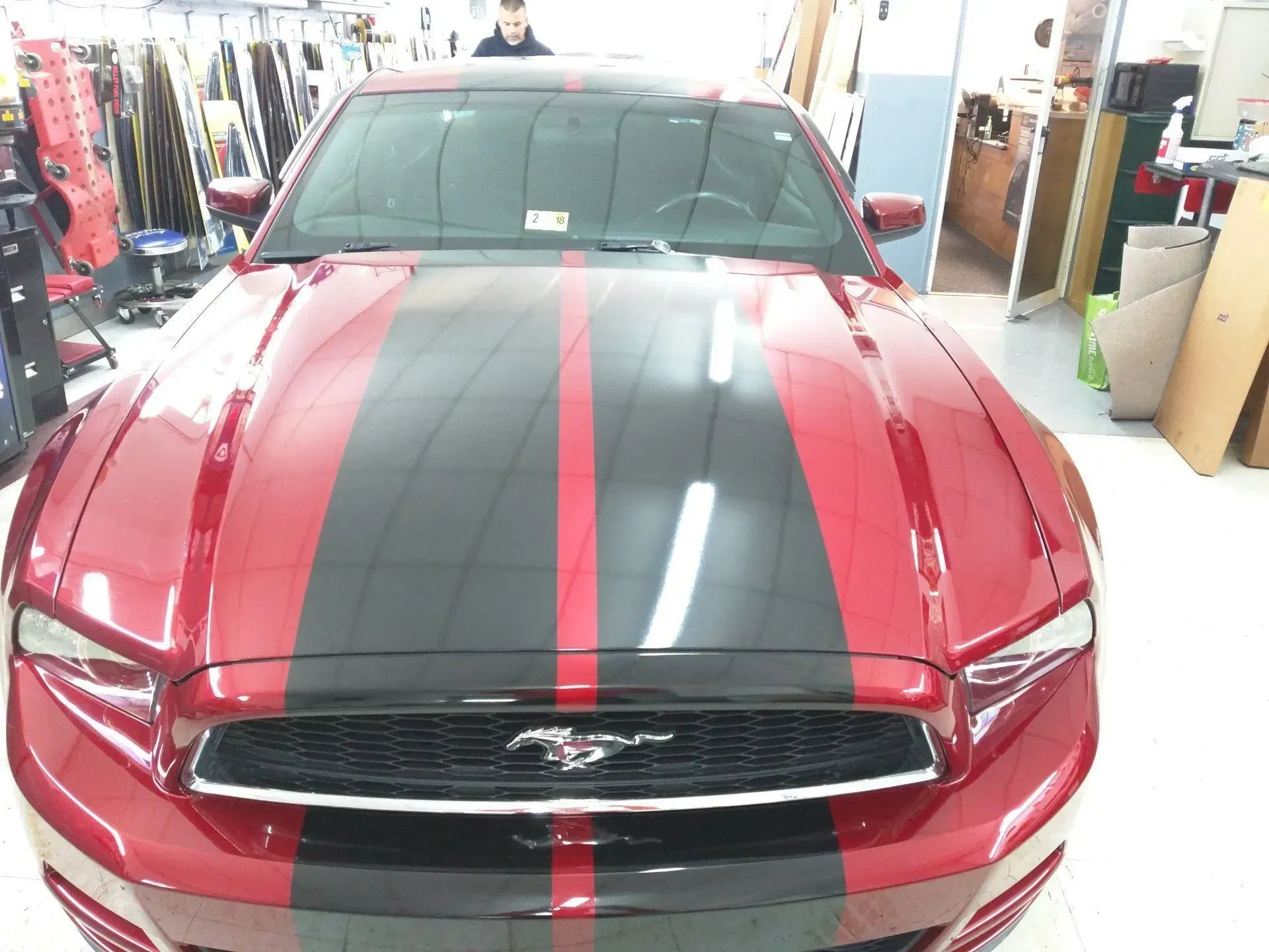 A red mustang with black stripes on the hood.