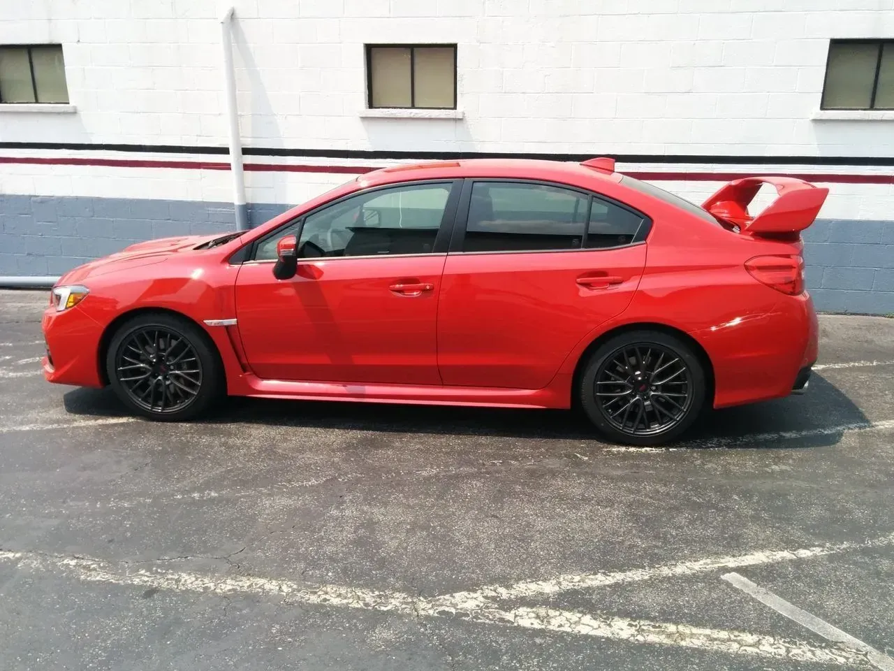 A red car is parked in a parking lo.t in front of a white building.
