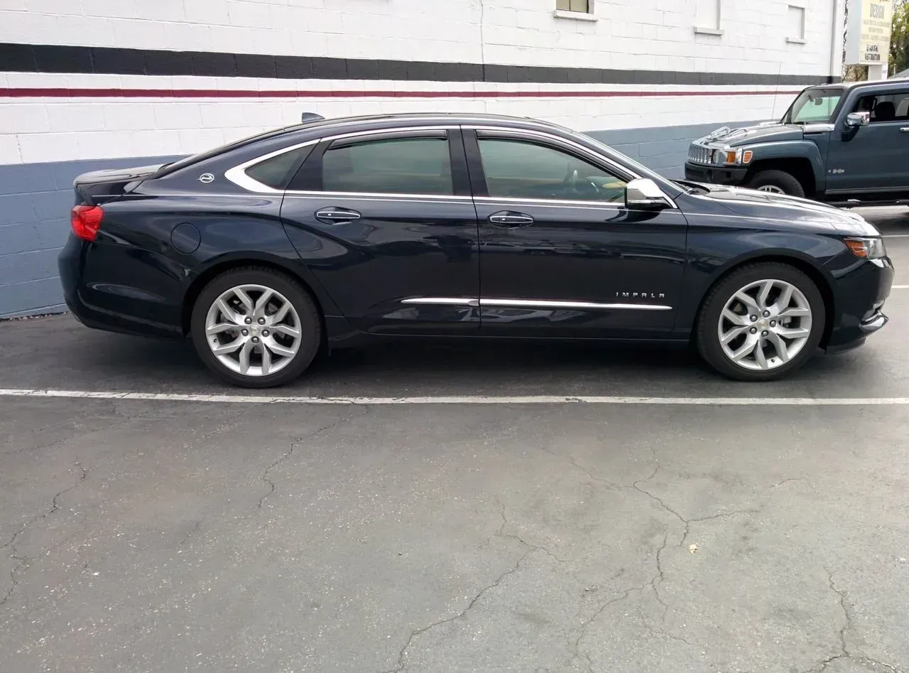 A black car is parked in a parking lot next to a jeep.