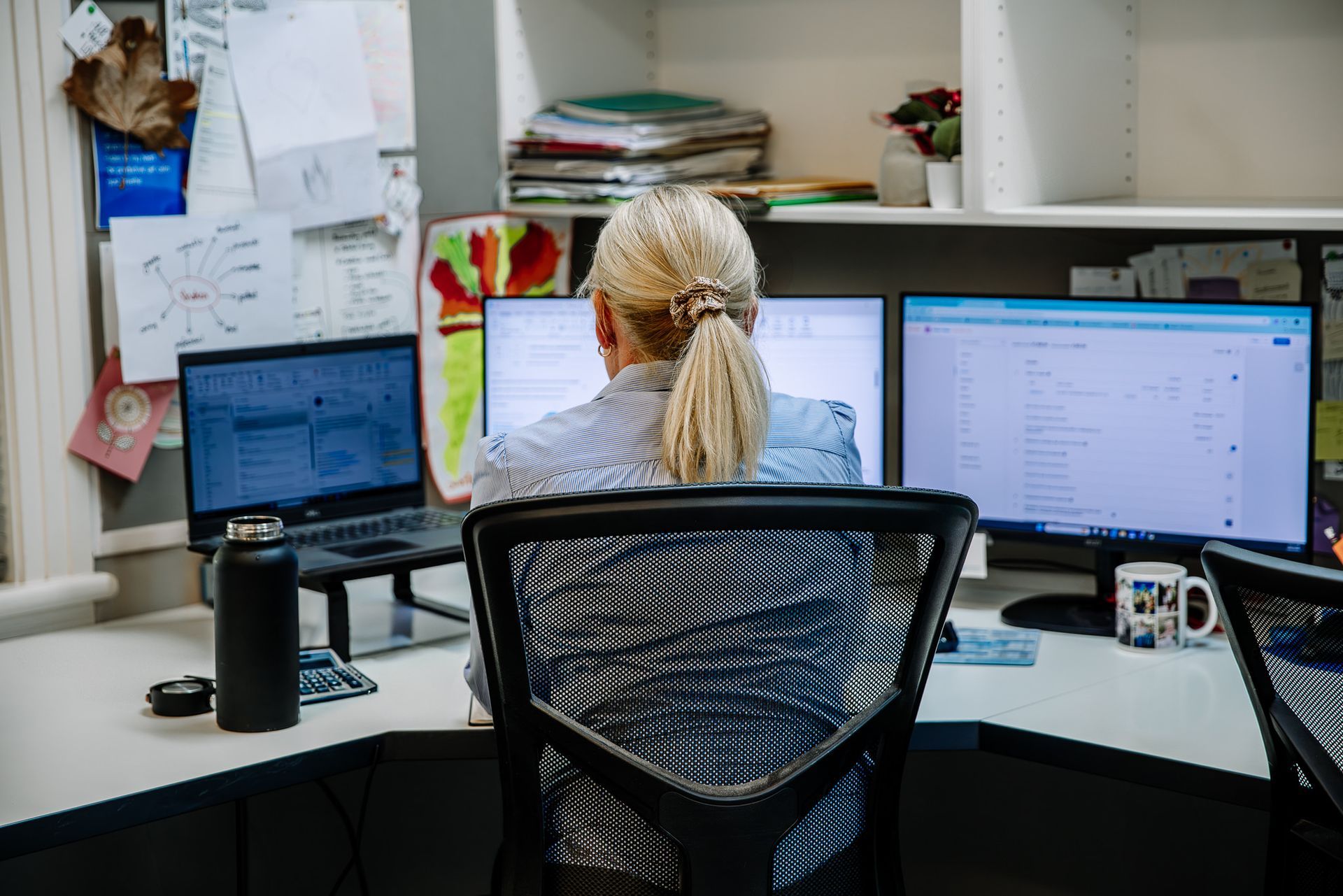 Person working at a desk with three computer monitors in an office cubicle