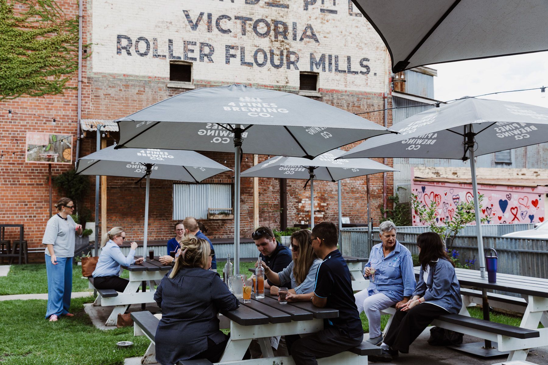 People seated at picnic tables under umbrellas outside Victoria Roller Flour Mills