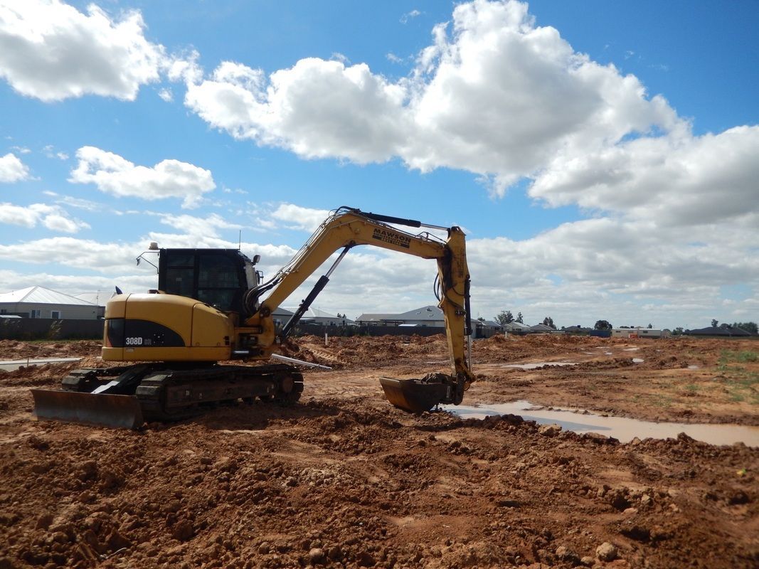 A Yellow Excavator is Digging a hole in a dirt field — Mawson Constructions in Kialla, VIC