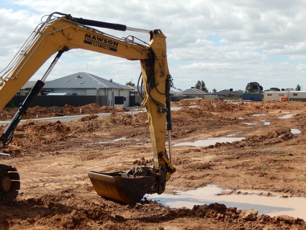 A Yellow Excavator is Digging a hole in a dirt field — Mawson Constructions in Kialla, VIC